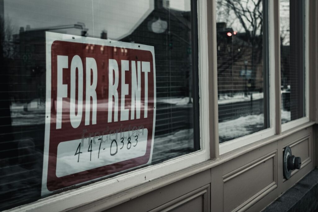 A person sits at a kitchen table reviewing bills and a rental agreement with a worried expression.